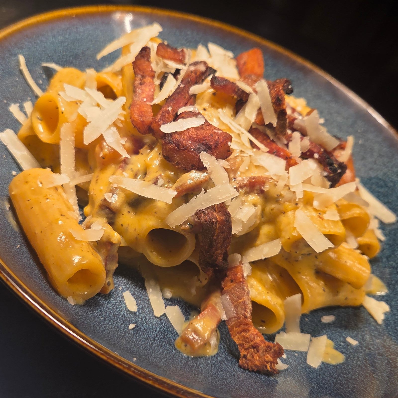 Rigatoni carbonara in a glossy egg and guanciale sauce, topped with shaved parmesan and crisp guanciale