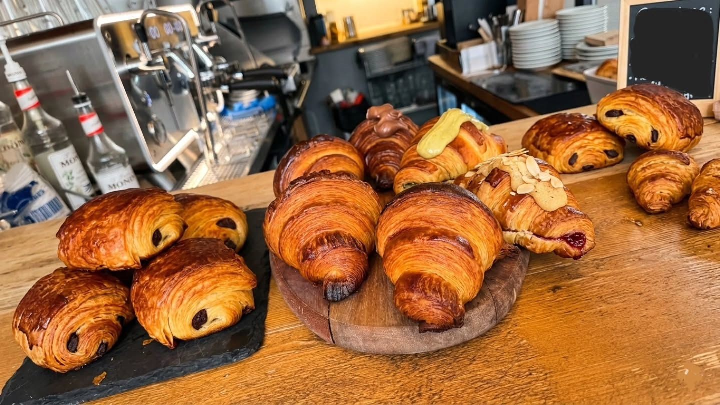 Freshly baked cornetti and pain au chocolat on wooden boards along the coffee bar, espresso machine behind