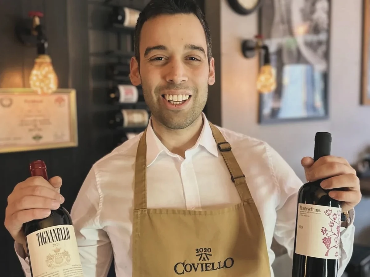 Daniel holding two bottles of Italian red wine behind the bar at Coviello