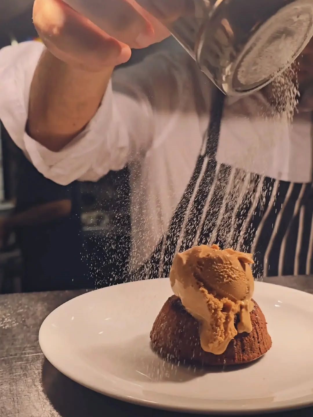 Warm chocolate fondant with caramel gelato, being dusted with icing sugar
