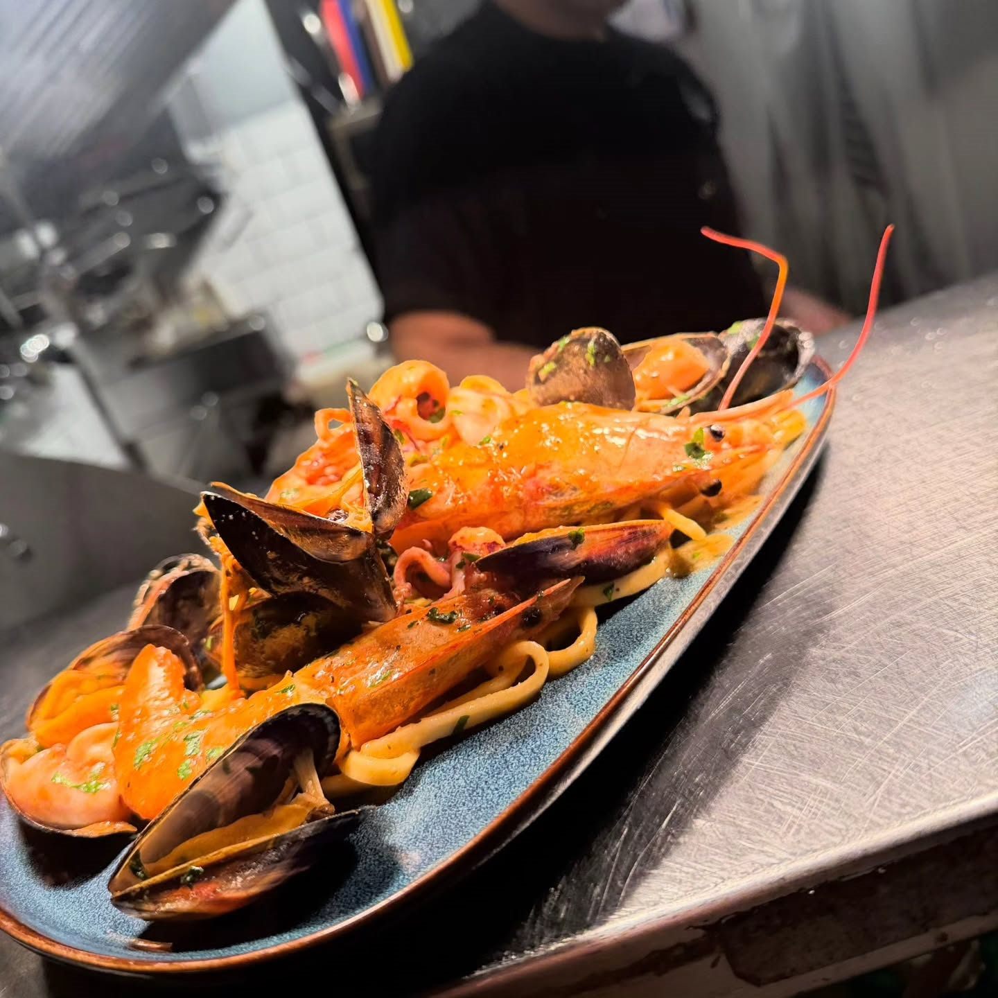 Linguine with mussels, prawns and squid in a light tomato sauce, plated on the pass