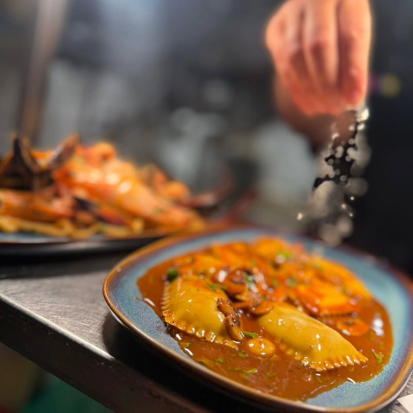 Ravioli filled with braised beef in a red wine sauce with sautéed mushrooms, being finished on the pass