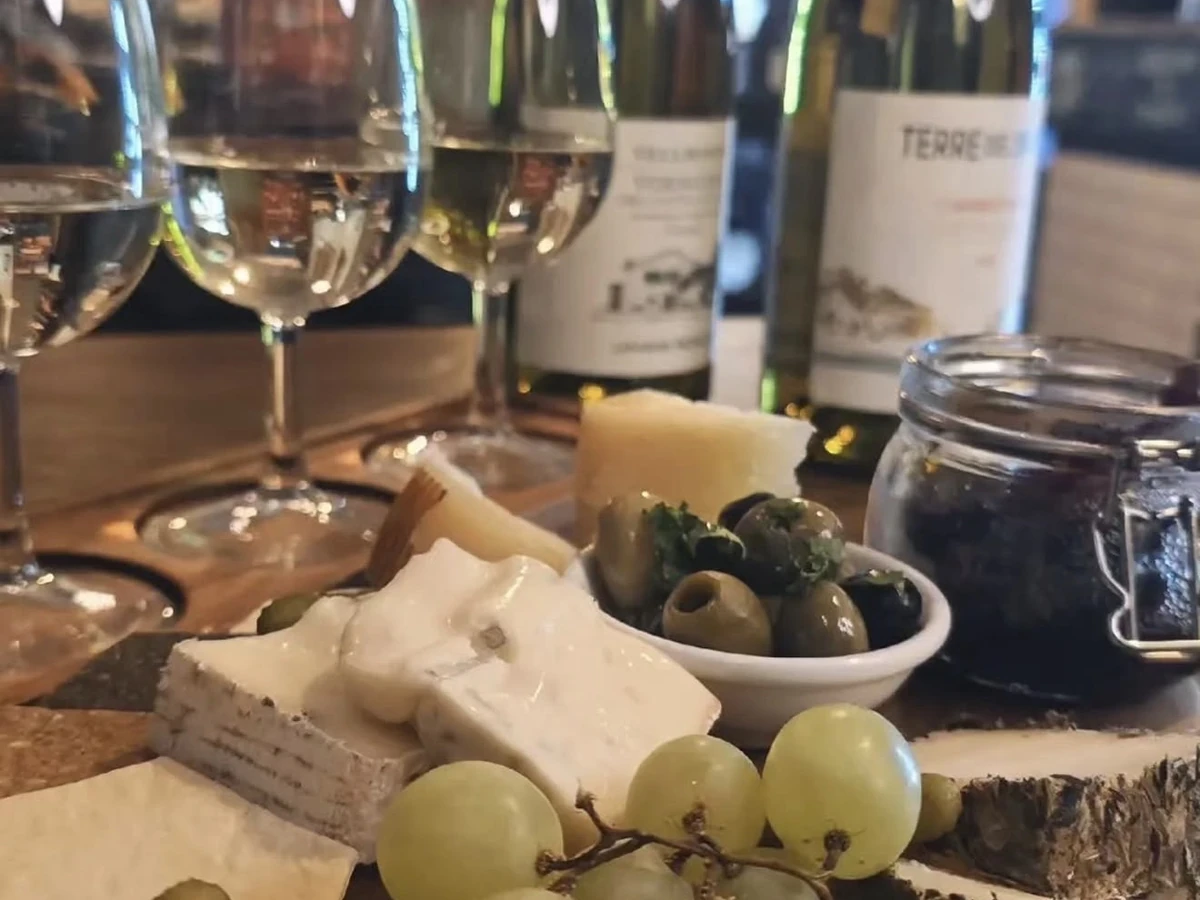 A flight of white wines poured beside a board of Italian cheeses and olives